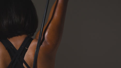 Close-Up-Studio-Shot-Of-Mature-Woman-Wearing-Gym-Fitness-Clothing-Exercising-With-Resistance-Band-Viewed-From-Behind